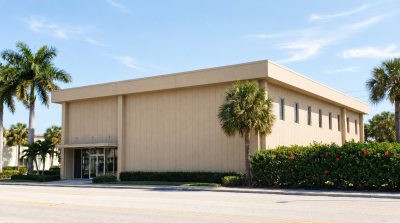 Florida approved wall panels on a two-story coastal office building, flat sand beige textured steel panels with thin vertical joints and royal palms out front